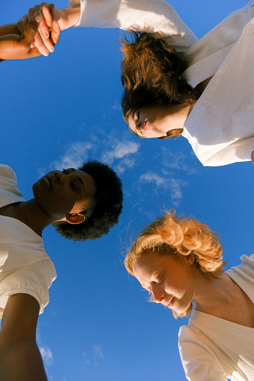 Céu azul, três mulheres de mãos dadas